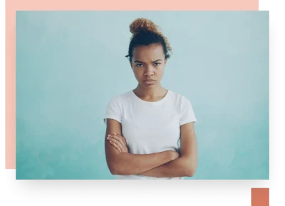 teenage mixed race girl with frizzy hair looking disgruntled at camera in front of light aqua blue background wall